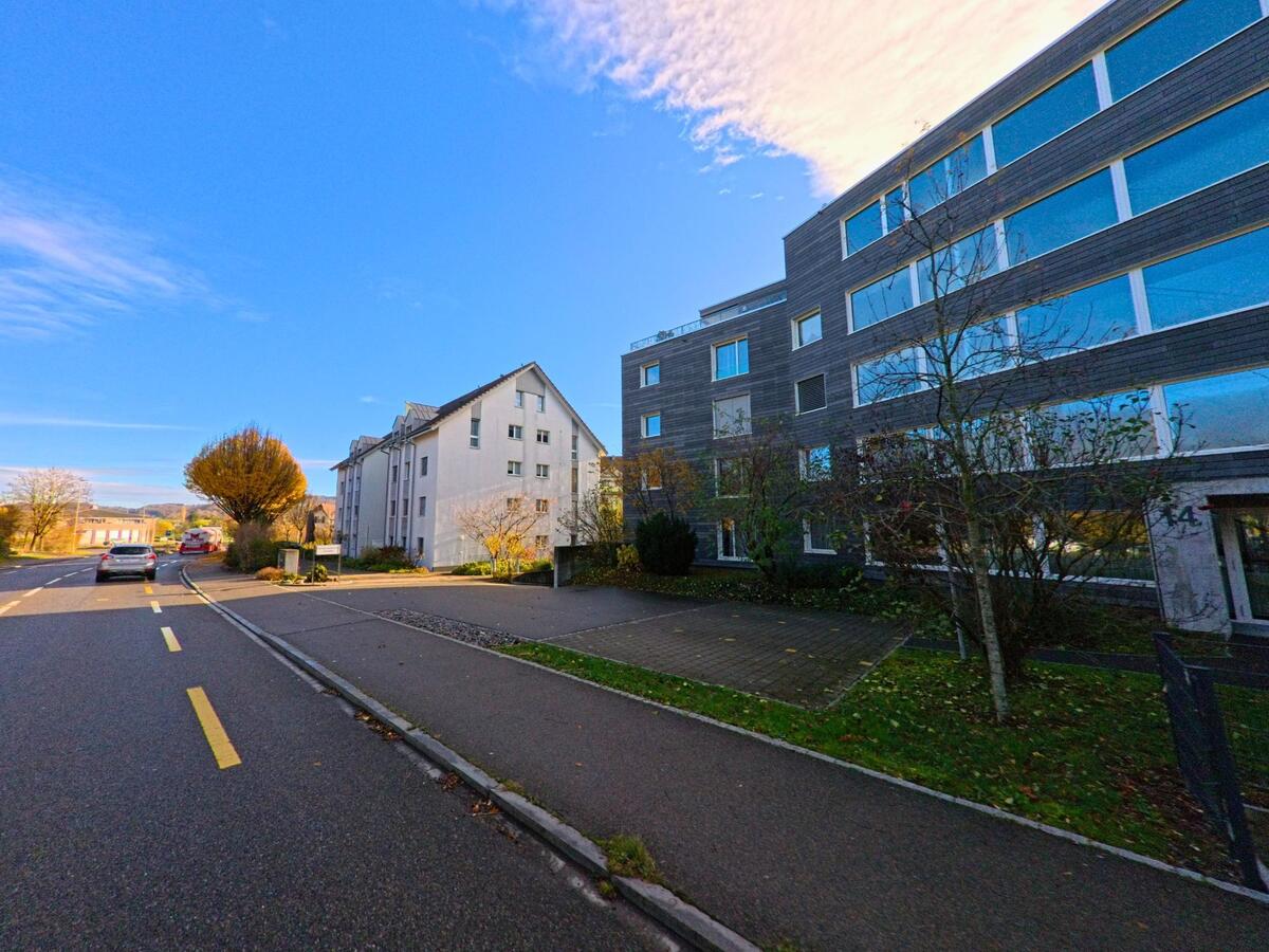 Entlang einer ruhigen Quartierstrasse in Münchwilen (9542, Kanton Thurgau) stehen moderne Wohn- und Geschäftsbauten neben einem breiten Trottoir.