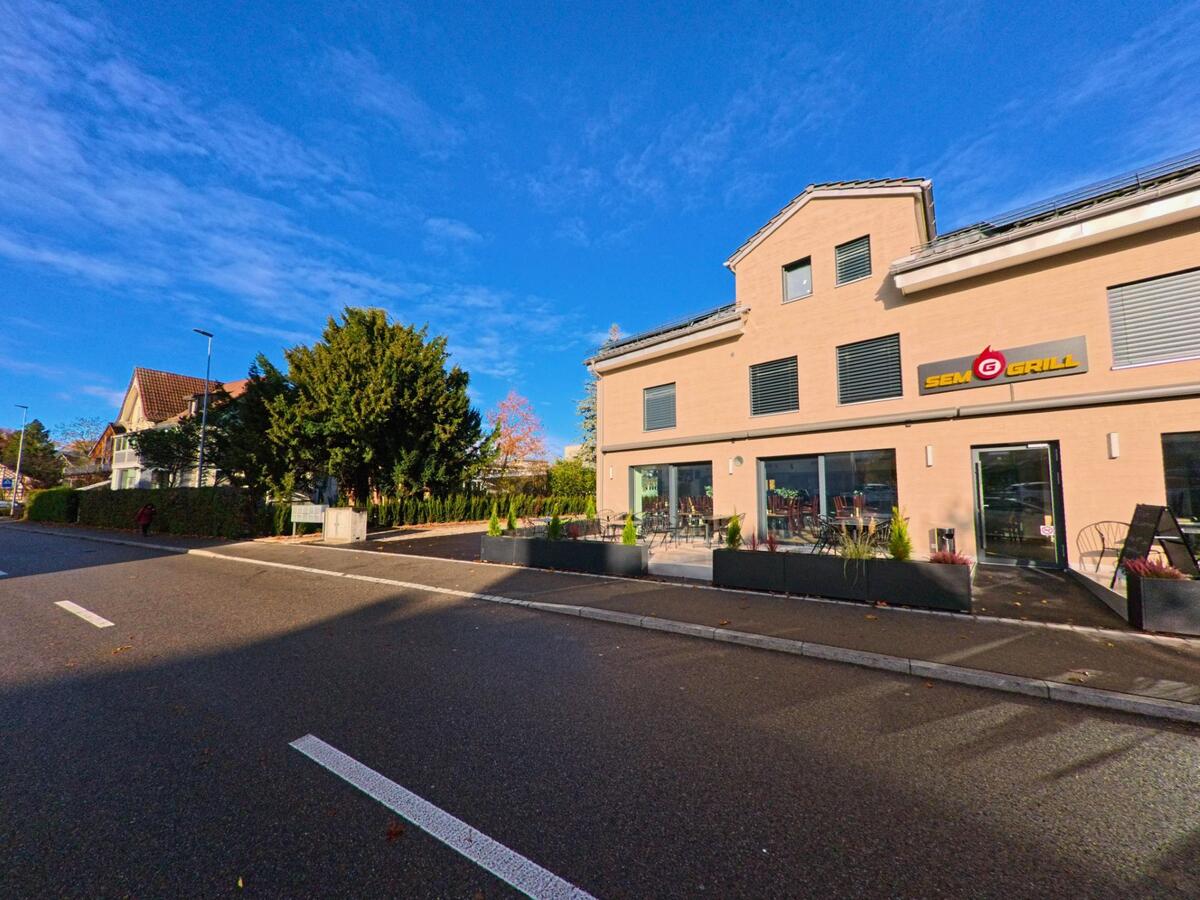 An der Strasse in Münchwilen (9542, Kanton Thurgau) liegt ein modernes Restaurantgebäude mit Terrasse und Pflanztrögen im warmen Sonnenlicht.