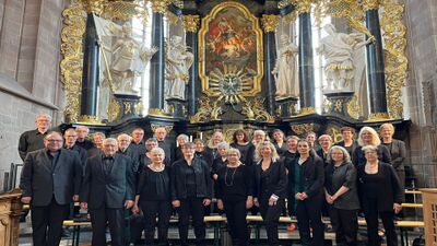 Der Münsterchor Bad Zurzach (Kanton Aargau) steht in schwarzer Kleidung vor einem reich verzierten Altar mit goldenen Ornamenten und Statuen.