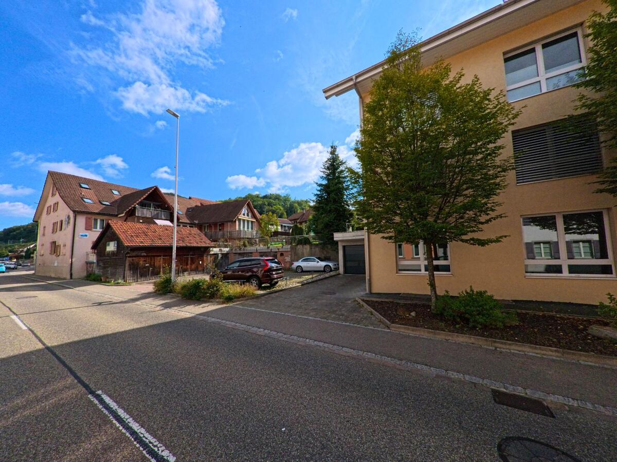 Eine ruhige Strasse in Mumpf (4322, Kanton Aargau) zeigt Wohnhäuser mit verschiedenen Fassaden und kleinen Vorgärten bei sonnigem Wetter.