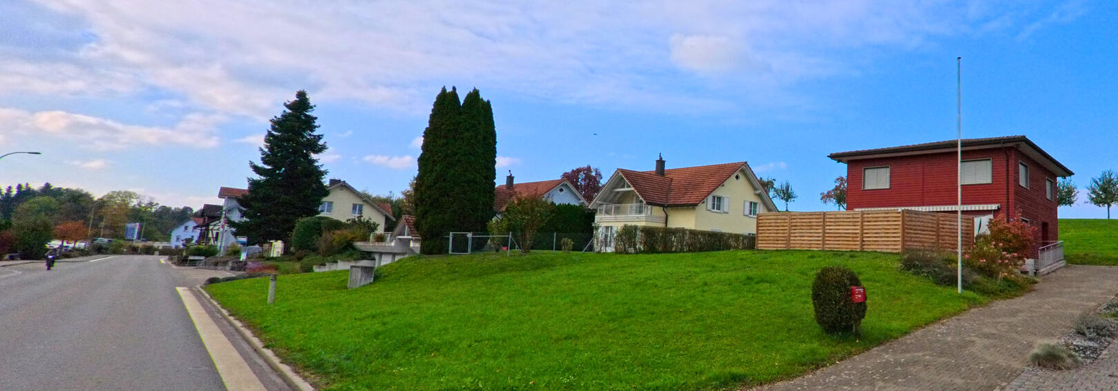 In Muolen (9313, Kanton St. Gallen) liegt eine Reihe gepflegter Einfamilienhaeuser an einer leicht ansteigenden Strasse, umgeben von gruener Wiese und einzelnen Baumen.
