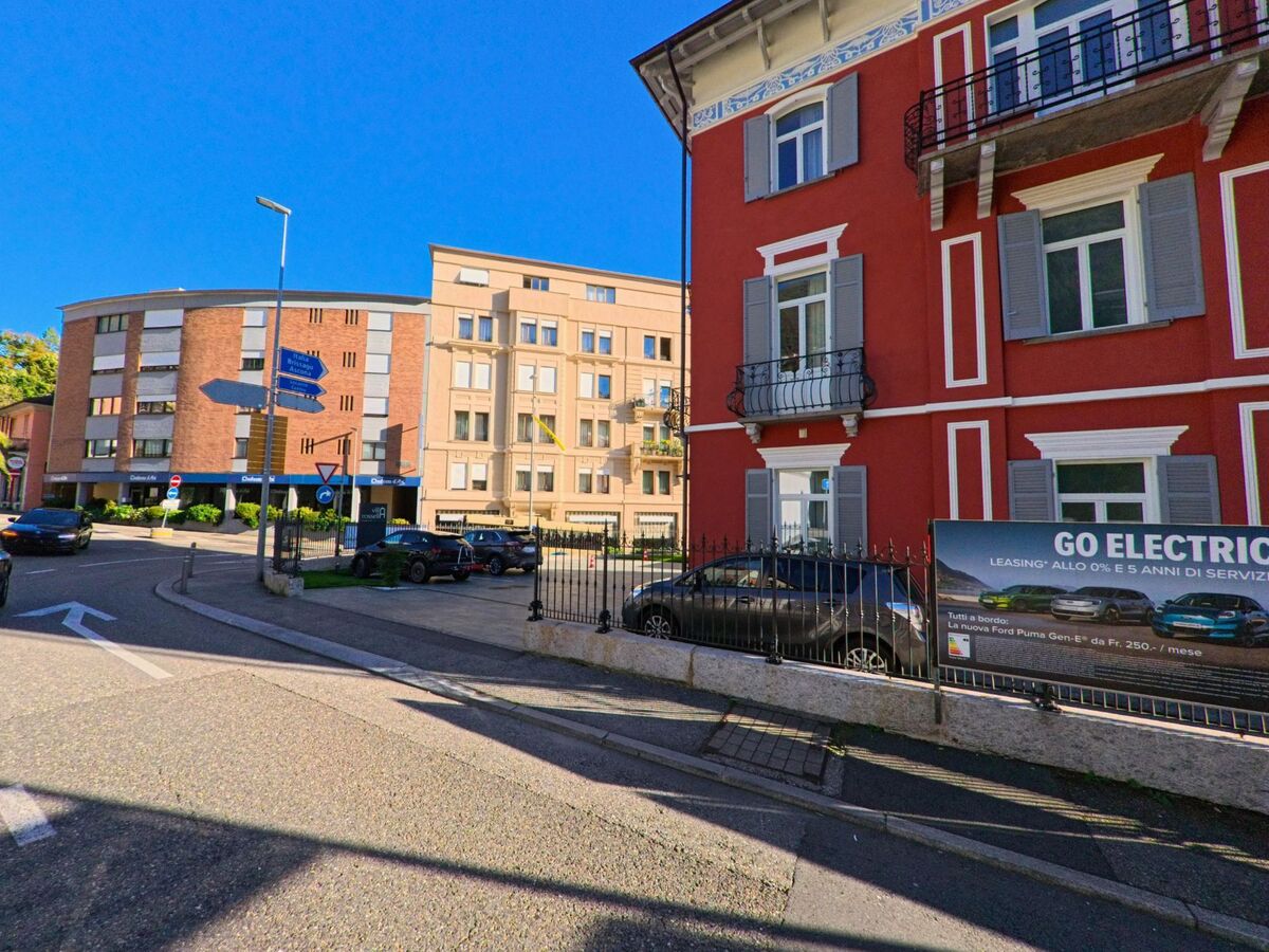 An einer Kreuzung mit unterschiedlichen Wohn- und Geschaeftsbauten zeigt sich ein Strassenbild in Muralto (6600, Kanton Tessin) bei klarem Tageslicht.