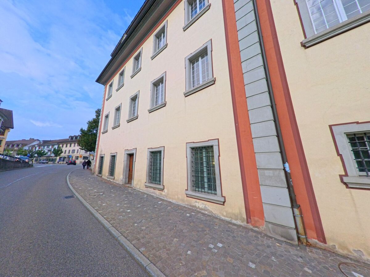 Eine gepflasterte Strasse mit historischen Gebaeuden fuehrt durch das Zentrum von Muri (5630, Kanton Aargau), wo Passanten entlang der Hausfassaden spazieren.