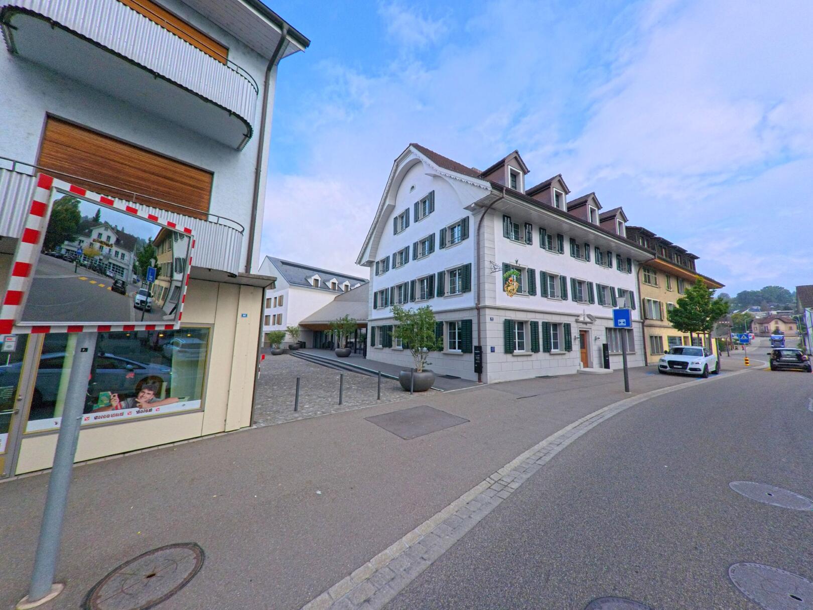 In der Gemeinde Muri (5630, Kanton Aargau) zeigt sich eine gepflegte Strasse mit dem traditionellen Gasthaus und mehreren Wohnhäusern unter blauem Himmel.