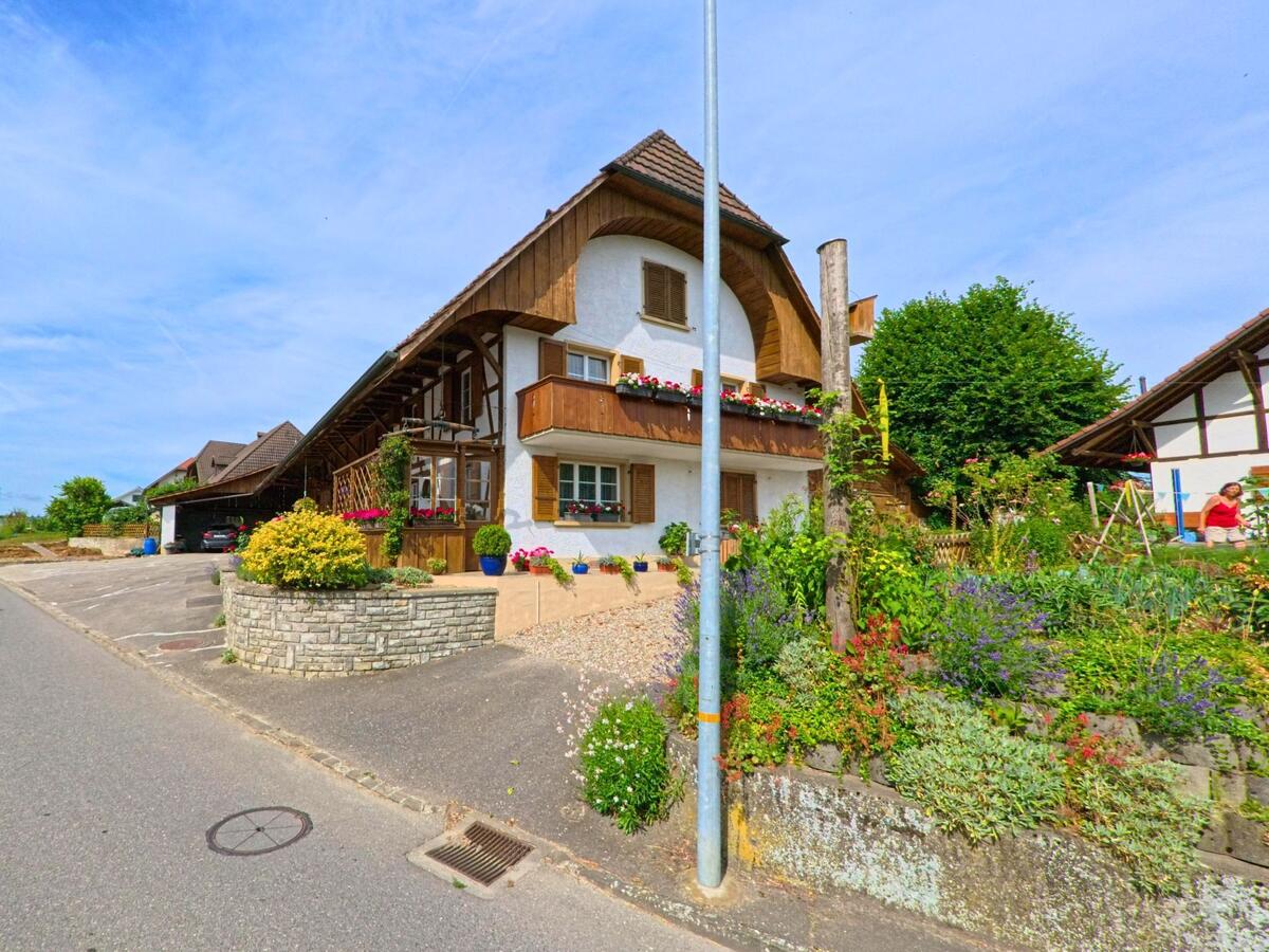 Ein gepflegtes Wohnhaus mit Holzbalkonen und farbenfroher Bepflanzung steht in Murten (3215, Kanton Freiburg) an einer ruhigen Quartierstrasse mit angrenzendem Gemüsegarten.