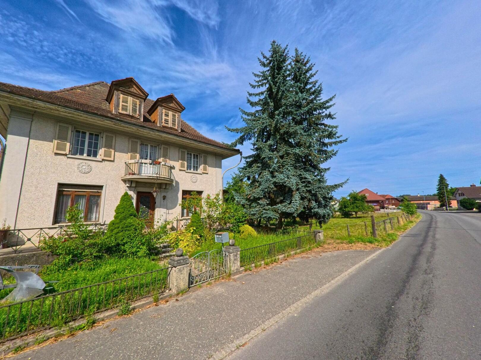 In Murten (3285, Kanton Freiburg) steht ein historisches Wohnhaus mit markantem Giebeldach und gepflegtem Vorgarten an einer ruhig verlaufenden Strasse.