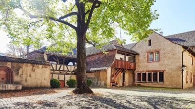 Im Museum Kleines Klingental in Basel (4058, Kanton Basel-Stadt) zeigt sich ein ruhiger Innenhof mit Kopfsteinpflaster, alten Mauern und einem grossen Baum im Sonnenlicht.