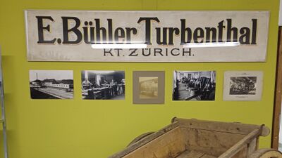 In Turbenthal (8488, Kanton Zuerich) zeigt eine Wand im Museum historische Fotografien und ein altes Schild der Firma E. Buehler Turbenthal aus frueheren Jahren.