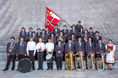 Eine Blasmusikgruppe in einheitlicher Kleidung mit Instrumenten und Fahne posiert auf einer Treppe in Safiental (7107, Kanton Graubuenden).