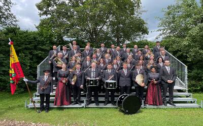 Die Musikgesellschaft Harmonie steht in Büsserach (4227, Kanton Solothurn) in festlicher Uniform auf einer Tribuene und praesentiert sich mit ihren Instrumenten im Freien.