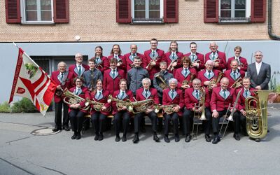 Mitglieder einer Musikgesellschaft in einheitlichen roten Uniformen sitzen und stehen mit Instrumenten fuer ein Gruppenfoto in Isenthal (6461, Kanton Uri).