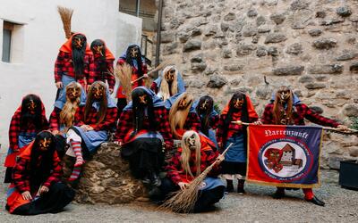Vor einer historischen Steinmauer steht in Stein am Rhein (8260, Kanton Schaffhausen) eine Gruppe maskierter Hexen in traditionellen Fasnachtskostuemen mit Besen und Banner.