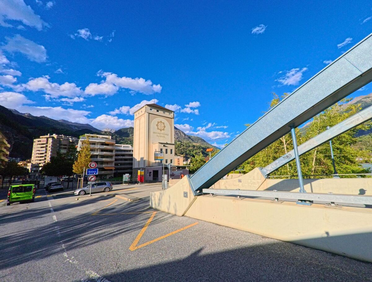 Der markante Turm mit der Aufschrift „Bienvenue a Naters“ praegt das Stadtbild von Naters (3900, Kanton Wallis), im Vordergrund ist ein Teil einer modernen Bruecke zu sehen.