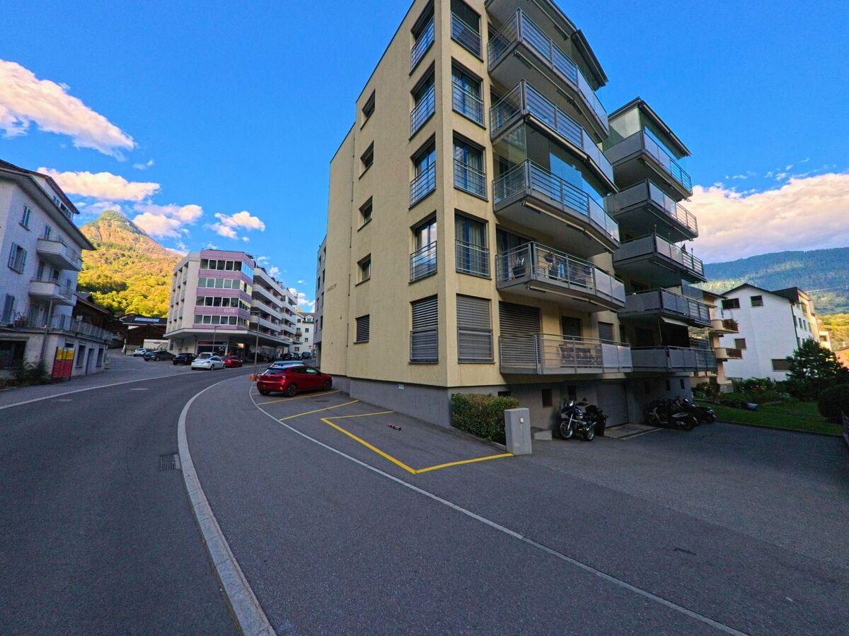Entlang einer leicht gekruemmten Strasse in Naters (3904, Kanton Wallis) stehen mehrgeschossige Wohngebaeude mit Balkonen und parkenden Fahrzeugen.
