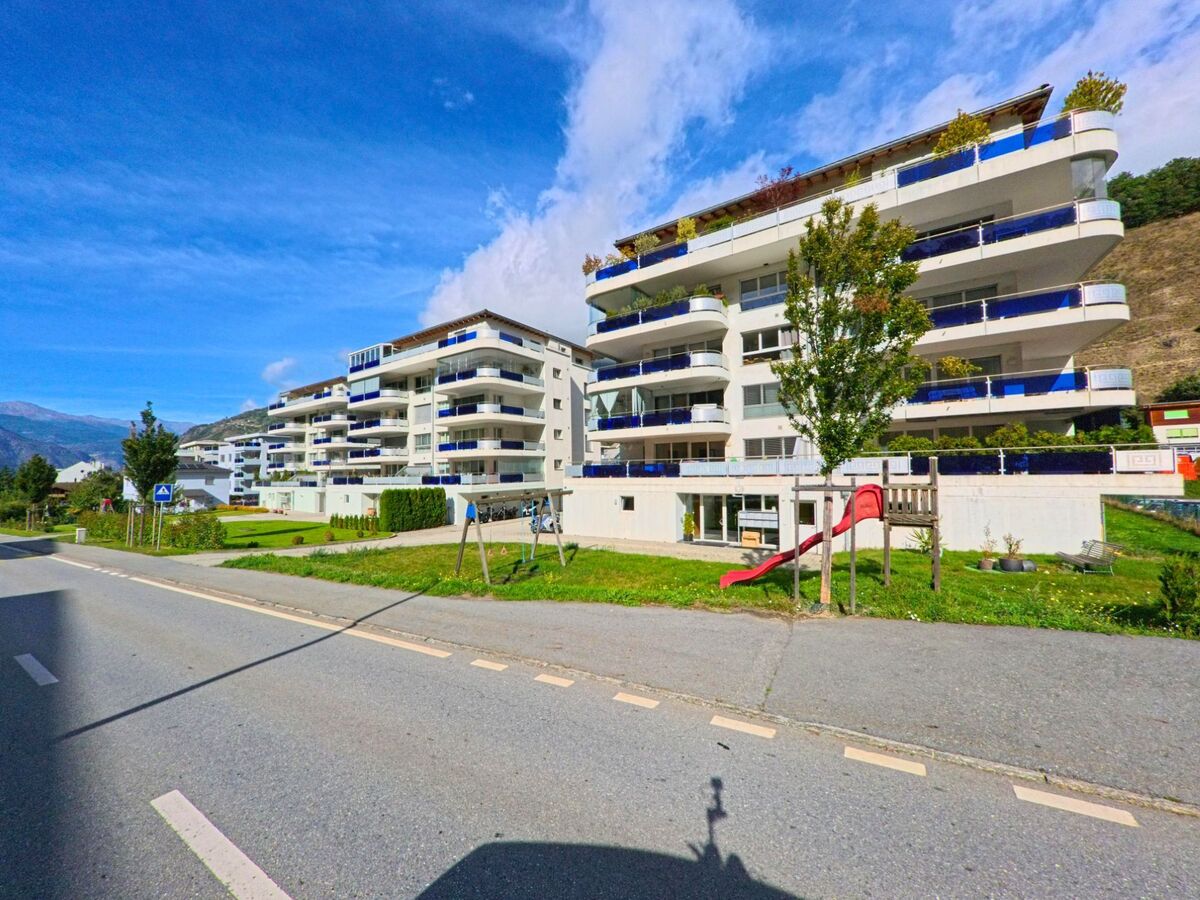 Vor modernen Wohnanlagen in Naters (3904, Kanton Wallis) liegt ein kleiner Spielplatz mit Rutsche und Schaukeln direkt an einer Quartierstrasse.