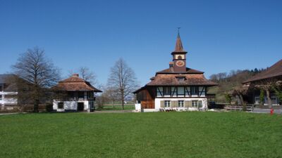 Das Nationale Milchwirtschaftliche Museum in Kiesen (3629, Kanton Bern) befindet sich in einem historischen Fachwerkhaus mit Uhrturm und liegt inmitten grüner Wiesen.