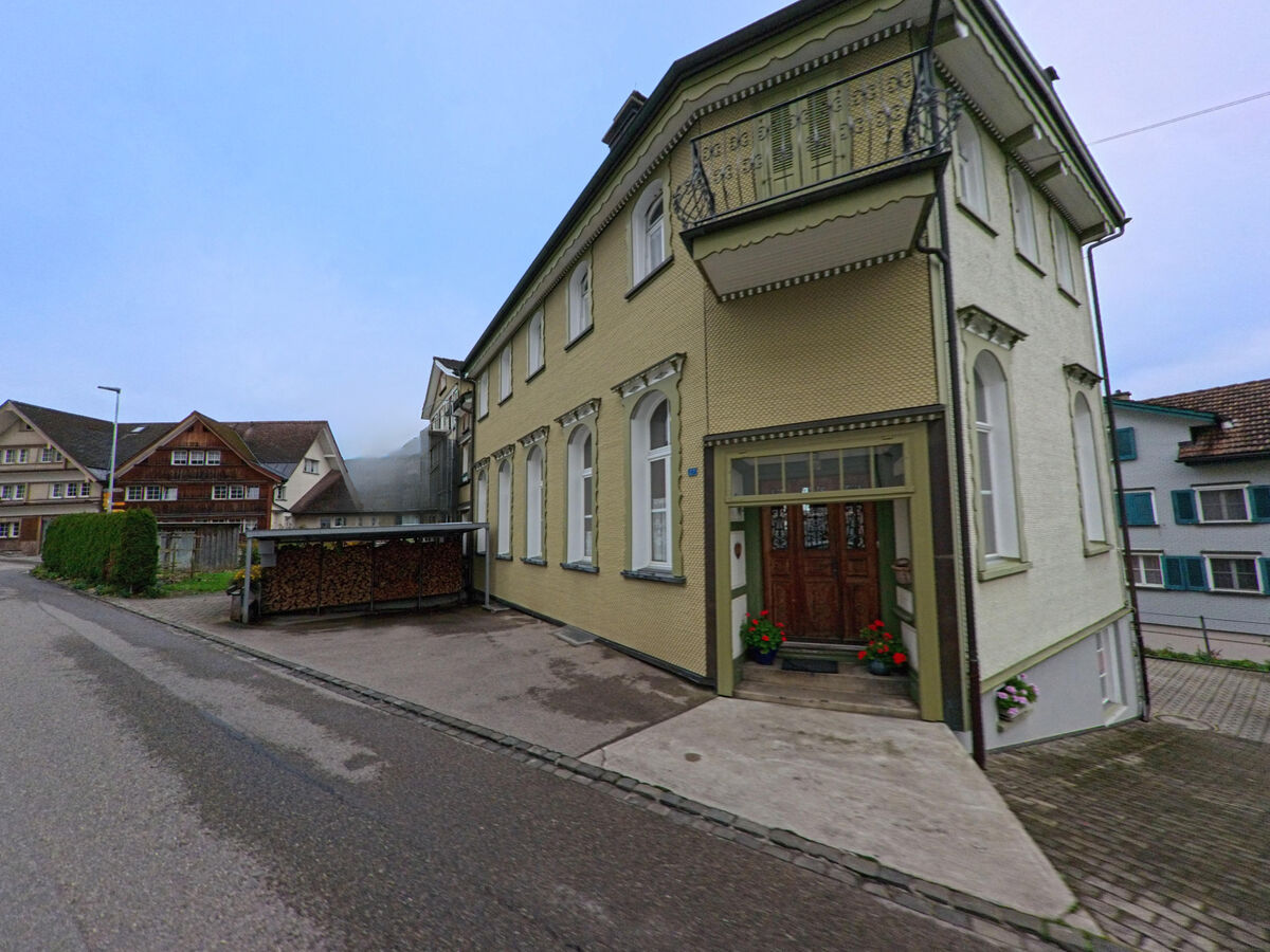 Ein verziertes Eckgebaeude mit Balkon steht an einer schmalen Strasse im Ort Neckertal (9122, Kanton St. Gallen).