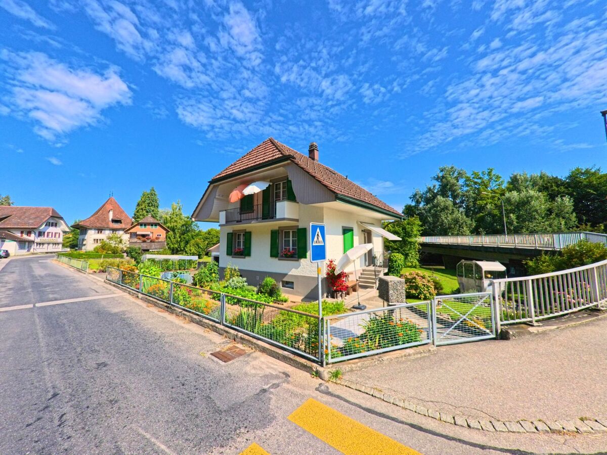 Ein Wohnhaus mit Garten und gruenen Fensterlaeden steht in Neuenegg (3176, Kanton Bern) nahe einer Fussgaengerbruecke.