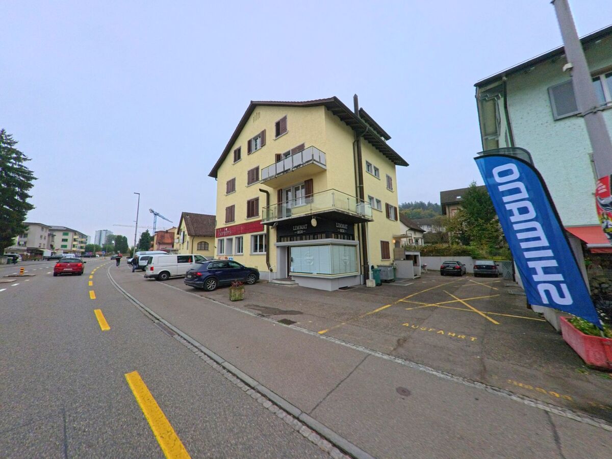 Ein gelbes Wohn- und Geschaeftshaus mit Balkonen steht an der Hauptstrasse in Neuenhof (5432, Kanton Aargau), vor dem mehrere Autos parken.