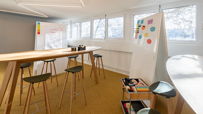 Ein moderner Arbeitsraum mit Stehtischen, Whiteboards und kreativen Materialien ist in Muttenz (4132, Kanton Baselland) hell und funktional eingerichtet.