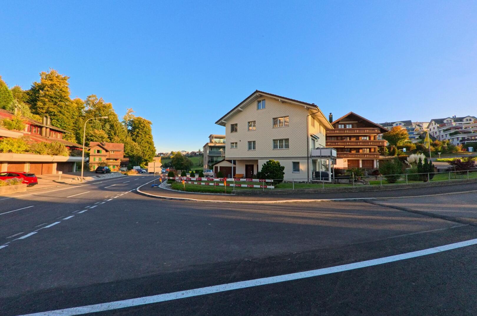 In Neuheim (6345, Kanton Zug) zeigt das Bild eine ruhige Strassenszene mit Wohnhaeusern, die im warmen Abendlicht vor blauem Himmel liegen.