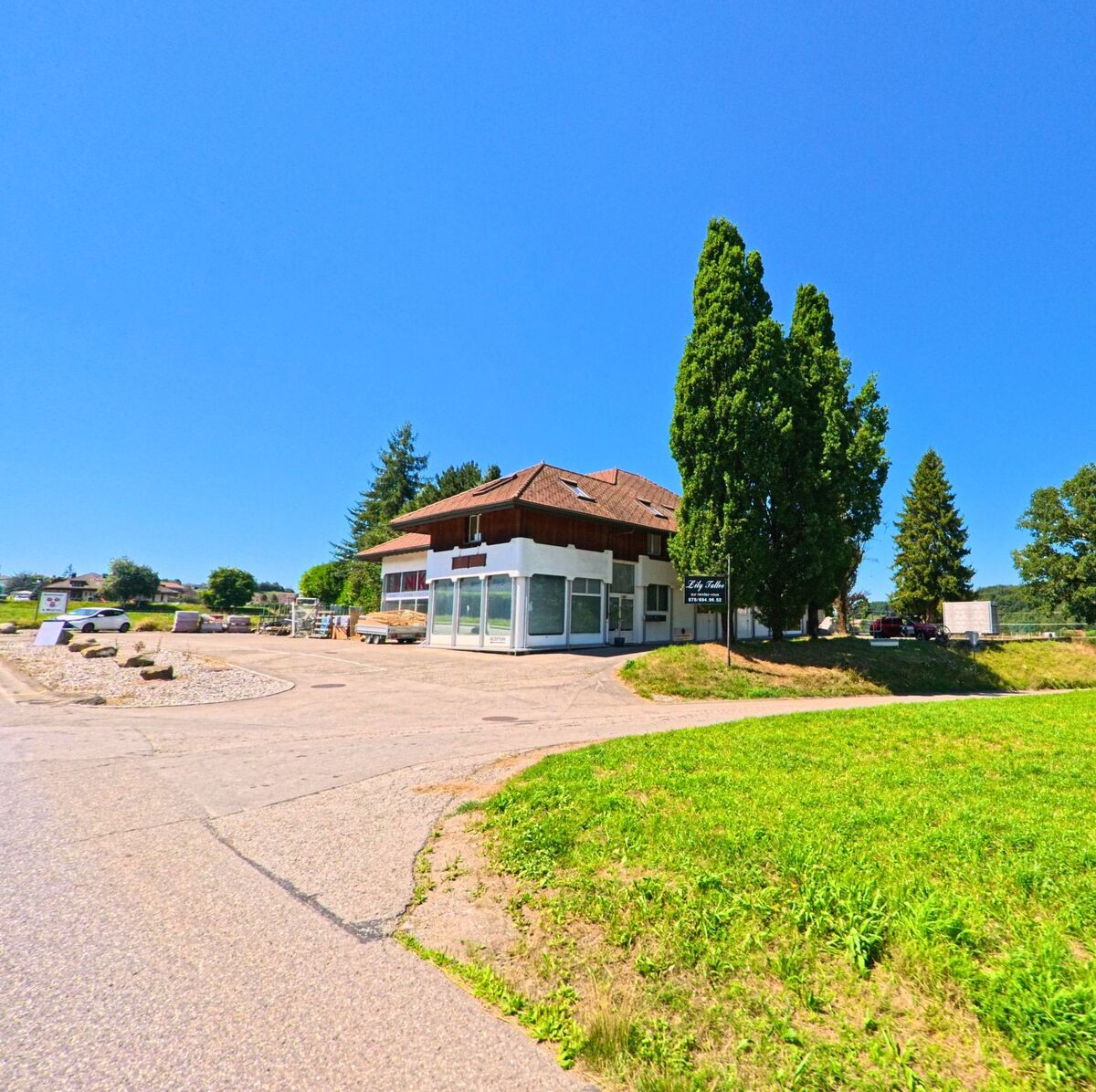 Am Ortsrand von Neyruz (1740, Kanton Freiburg) steht ein zweistöckiges Gebäude mit grosser Fensterfront, umgeben von Bäumen und einer weiten Grünfläche.