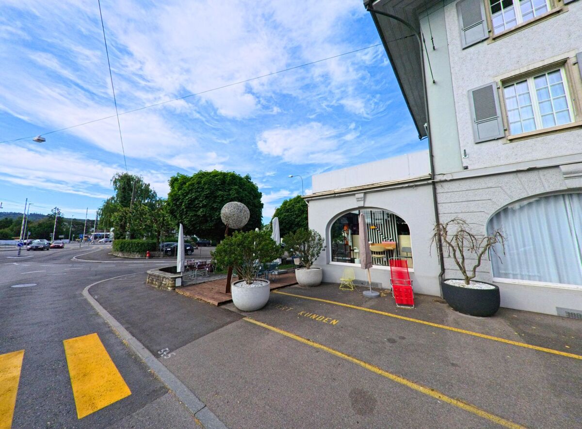 In Nidau (2560, Kanton Bern) ist die Straßenszene von einem modernen Gebäude und gepflegten Grünflächen geprägt, während die gelben Straßenmarkierungen auf den Kreisverkehr hinweisen.