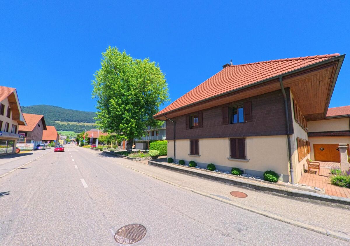 In Niederbipp (4704, Kanton Bern) saeumen traditionelle Wohnhaeuser mit roten Daechern eine breite Strasse mit Blick auf bewaldete Huegel.