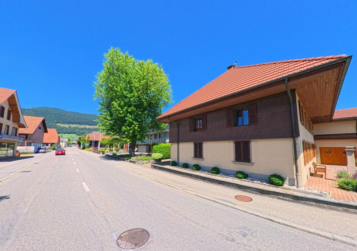 In Niederbipp (4704, Kanton Bern) saeumen traditionelle Wohnhaeuser mit roten Daechern eine breite Strasse mit Blick auf bewaldete Huegel.