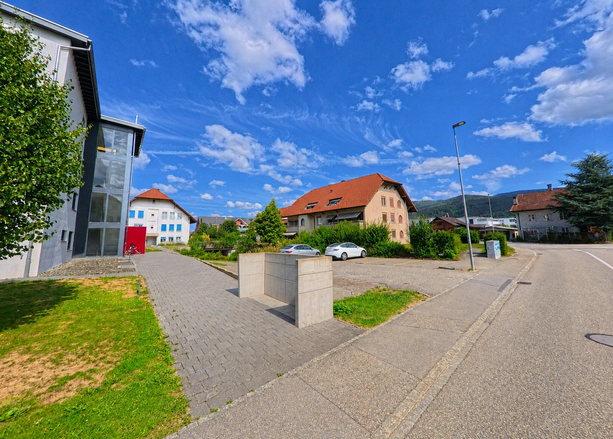 In Niederbuchsiten (4626, Kanton Solothurn) liegen Wohnhäuser und weitere Gebäude entlang einer ruhigen Strasse mit Parkplätzen, Grünflächen und Blick auf die bewaldete Hügellandschaft.