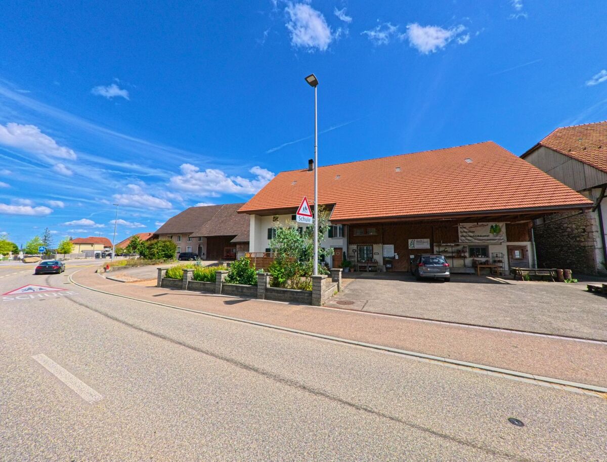 An der Hauptstrasse in Niederbuchsiten (4626, Kanton Solothurn) liegt ein Bauernhof mit Direktverkauf, grosszügigem Vordach und Hinweis auf eine nahegelegene Schule.