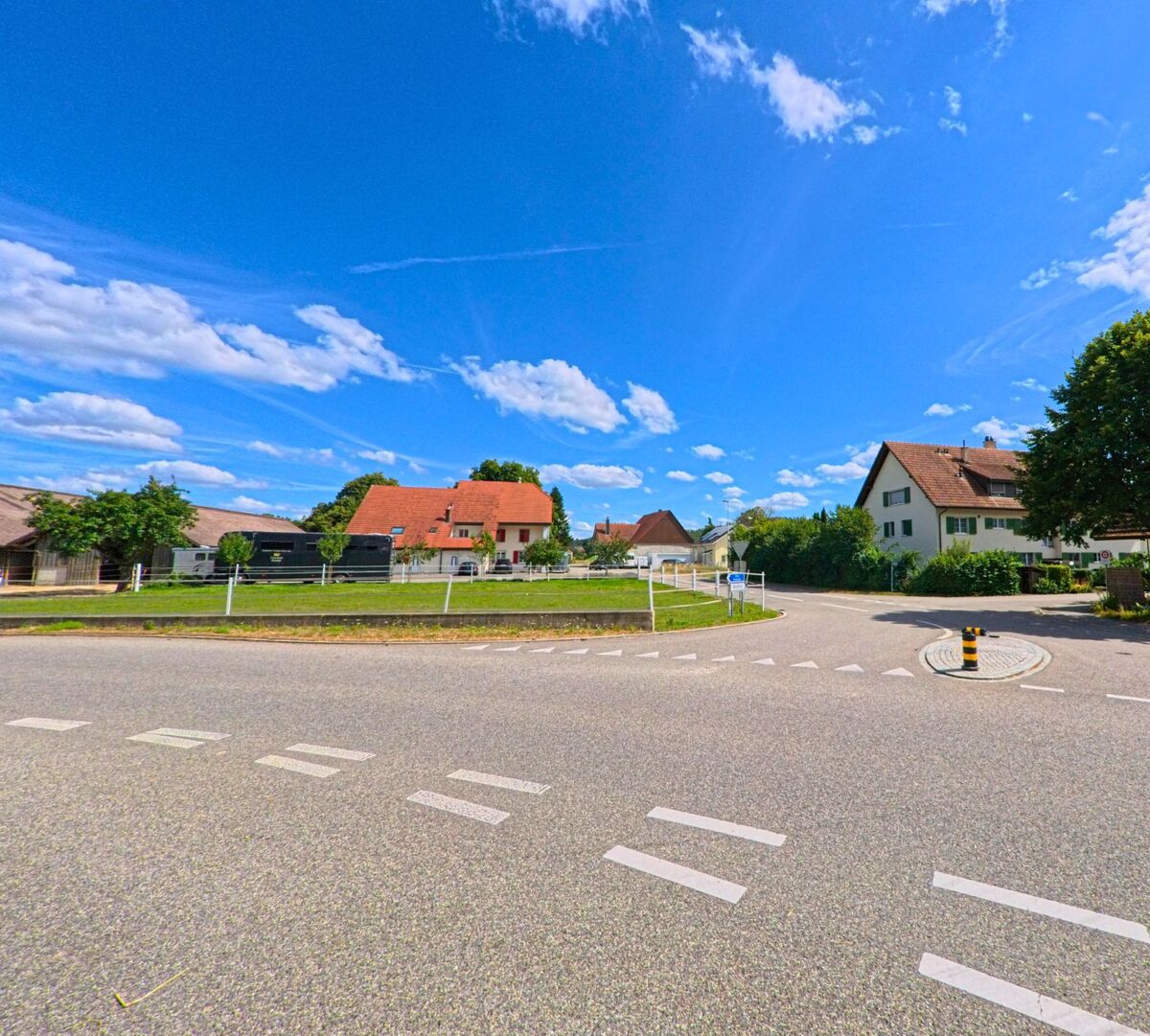 Am Rande einer Kreuzung in Niederbuchsiten (4626, Kanton Solothurn) befinden sich gepflegte Einfamilienhaeuser und ein eingezäuntes Grundstück mit Pferdeanhängern.