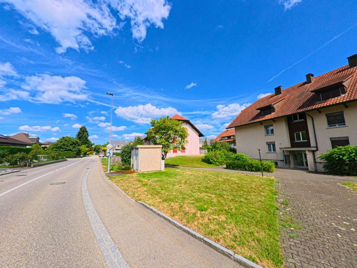 In Niederbuchsiten (4626, Kanton Solothurn) verläuft eine Wohnstrasse mit Mehrfamilienhaeusern und gepflegten Gruenflächen in Richtung des Ortszentrums.