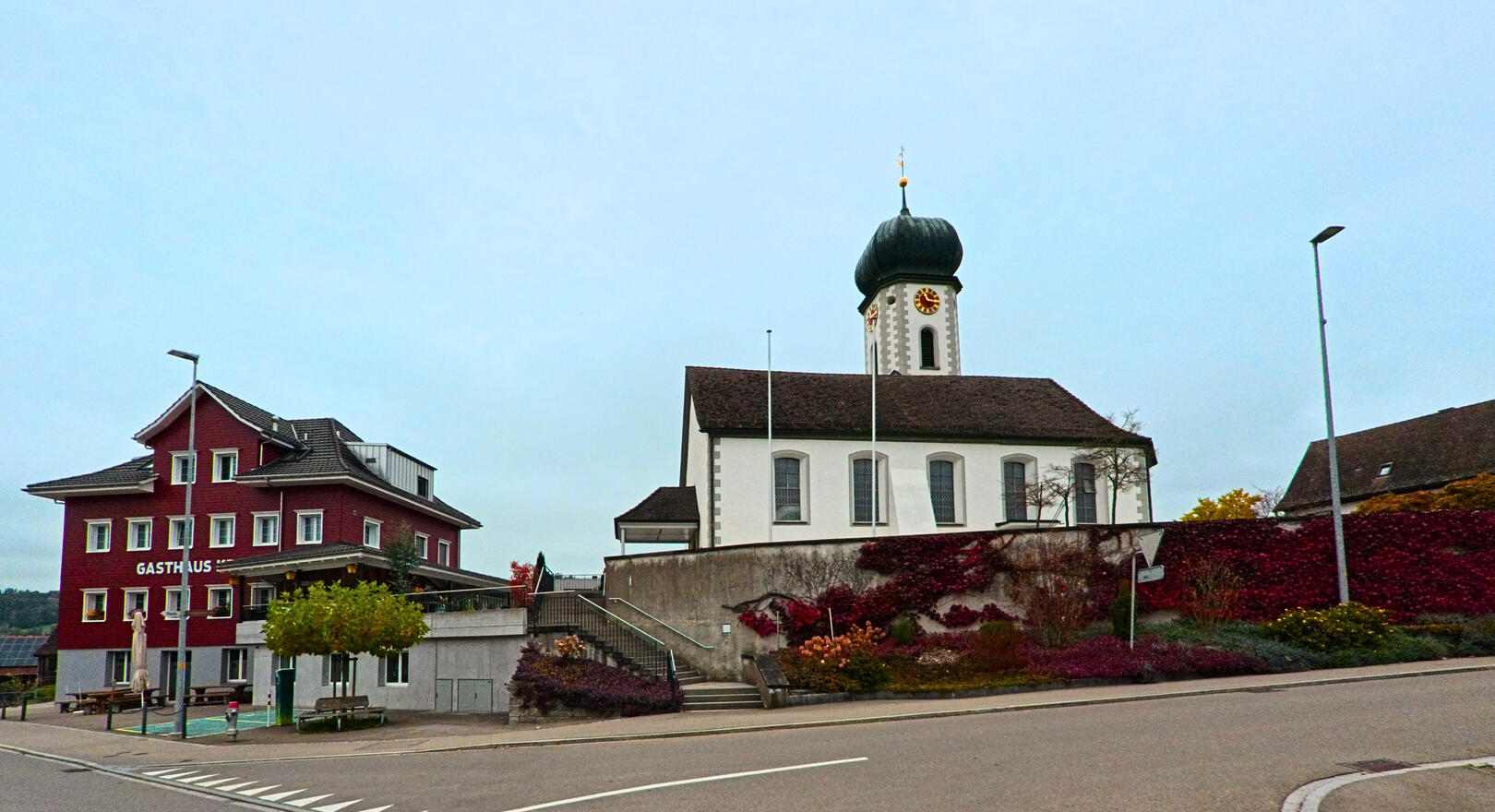 Neben einer Kirche mit markantem Turm liegt in Niederhelfenschwil (9527, Kanton St. Gallen) ein Gasthaus an einer leicht ansteigenden Strasse.