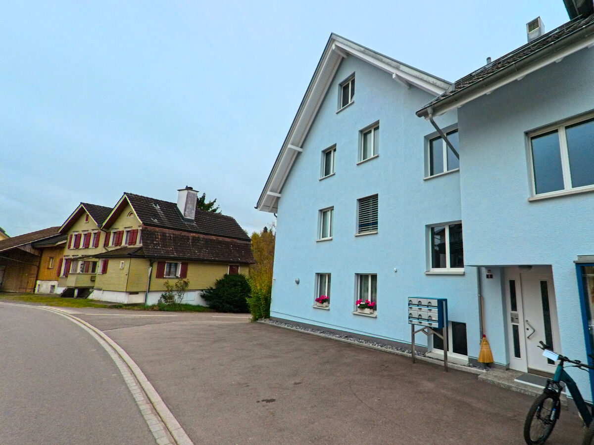 Ein helles Wohngebaeude steht nahe der Fahrbahn im Dorfgebiet von Niederhelfenschwil (9527, Kanton St. Gallen).