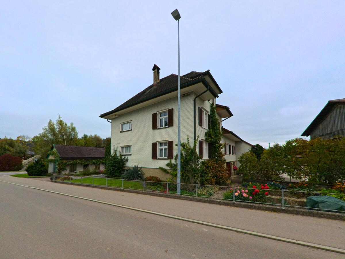 Ein Wohnhaus mit Vorgarten steht an einer leicht geschwungenen Strasse in Niederhelfenschwil (9527, Kanton St. Gallen).
