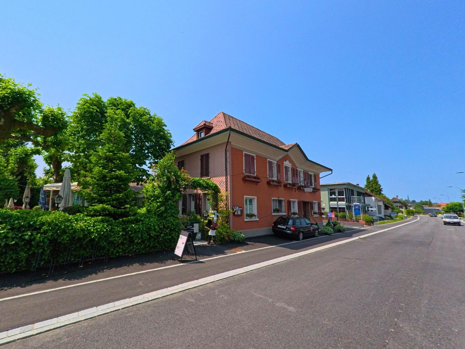 An der Hauptstrasse in Niederönz (3362, Kanton Bern) steht ein rosafarbenes Gebäude mit Fensterläden und Gastrobetrieb, daneben schattige Gartensitzplätze unter grossen Bäumen.