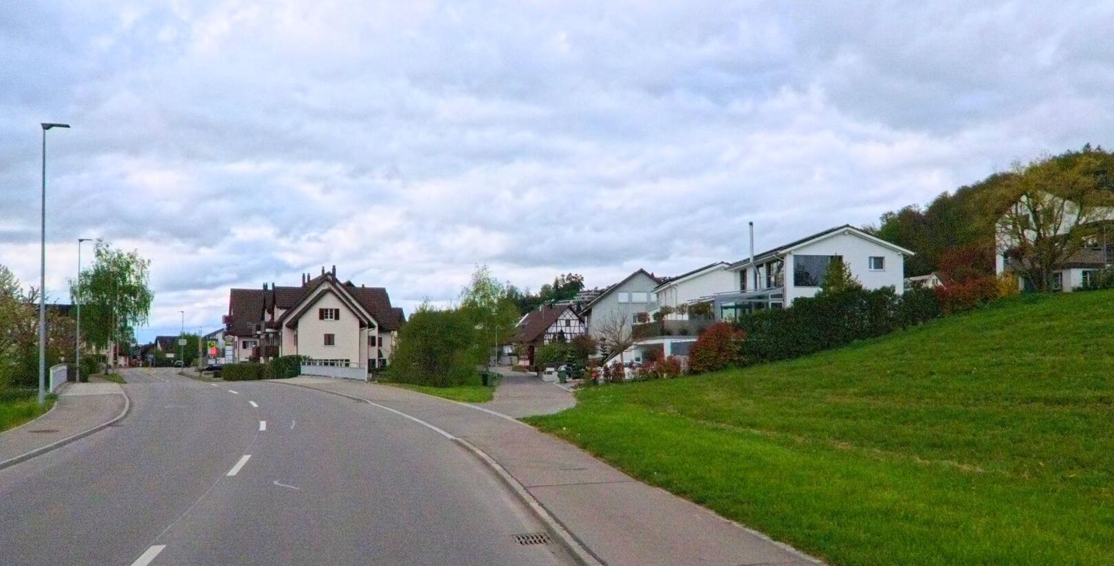 In Niederweningen, PLZ 8166 im Kanton Zürich, verläuft eine kurvige Hauptstrasse durch ein Wohnquartier mit Einfamilienhäusern am Hang.