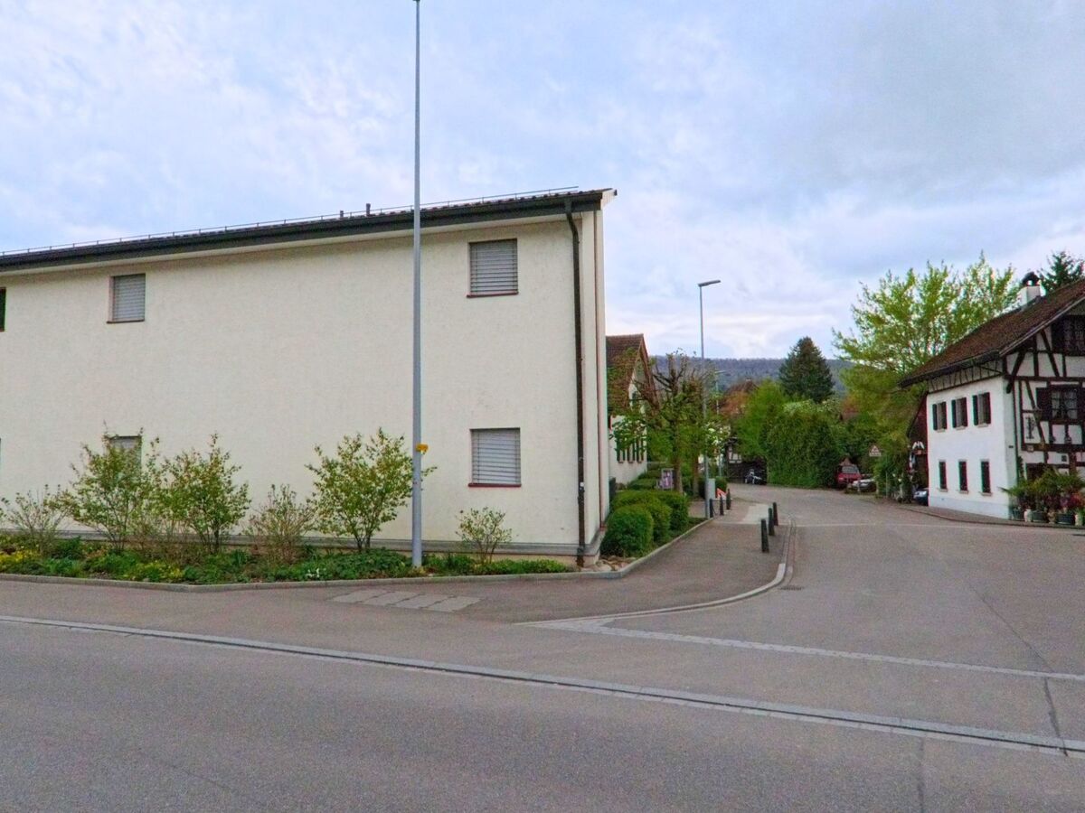 In Niederweningen, PLZ 8166 im Kanton Zürich, mündet eine Seitenstrasse mit gepflegter Bepflanzung zwischen einem modernen Wohnhaus und einem traditionellen Fachwerkgebäude.