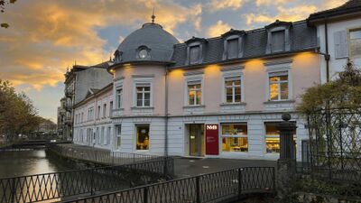 In Biel/Bienne (2501, Kanton Bern) liegt das NMB Neues Museum Biel an einem Kanal, in einem hellen Gebaeude mit Mansardendach und abendlicher Beleuchtung.