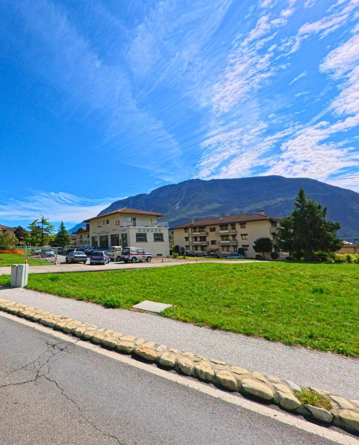 Ein Gebäude mit der Aufschrift Garage steht in Noble-Contrée (3968, Kanton Wallis) vor einer Wiese, im Hintergrund ragt ein bewaldeter Berg auf.