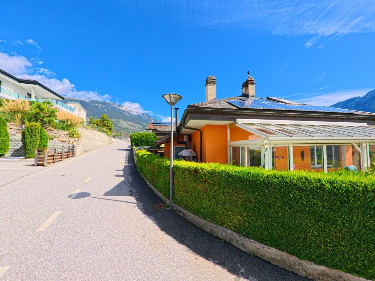 Ein Haus mit orangefarbener Fassade und Solarpanelen steht in Noble-Contrée (3968, Kanton Wallis) an einer ansteigenden Strasse.