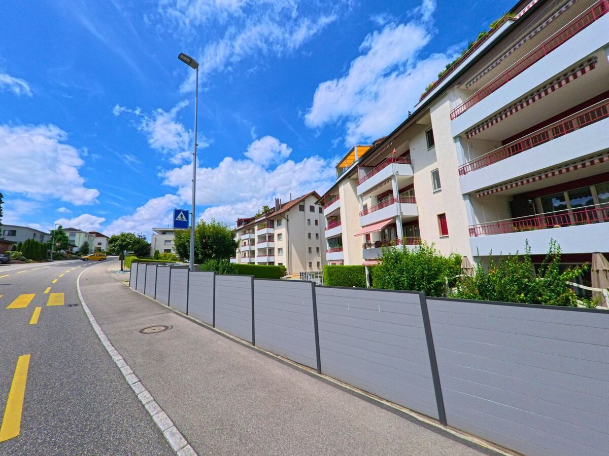 Mehrfamilienhaeuser mit grossen Balkonen und rot-weissen Markisen praegen das Bild entlang einer ansteigenden Strasse in Nottwil (6207, Kanton Luzern).