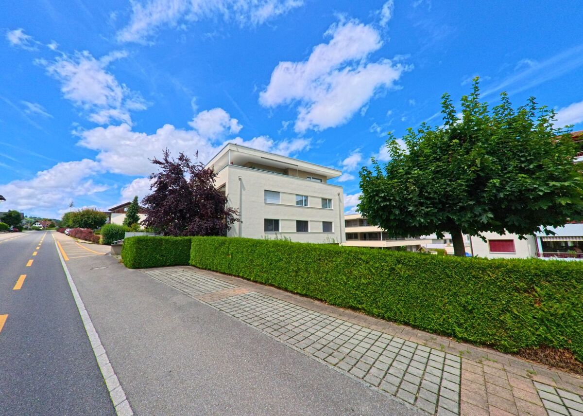 In Nottwil (6207, Kanton Luzern) steht ein modernes Wohnhaus mit flachem Dach hinter einer gepflegten Hecke entlang einer breiten Strasse.