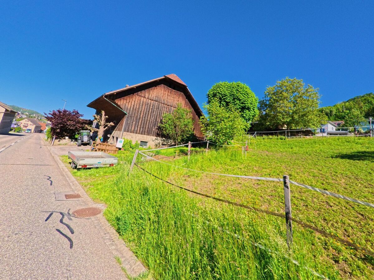 Am Rand von Nunningen (4208, Kanton Solothurn) steht eine Holzscheune neben einer eingezäunten Wiese unter strahlend blauem Himmel.