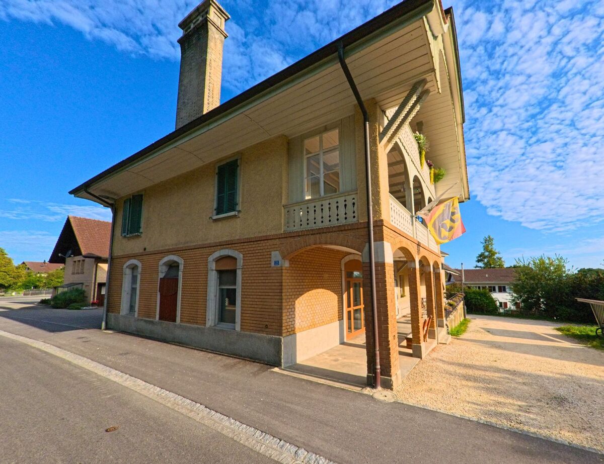 Ein zweigeschossiges Gebäude mit grossem Kamin in Oberbalm (3096, Kanton Bern) zeigt eine verzierte Fassade und trägt eine Fahne des Kantons Bern am Balkon.