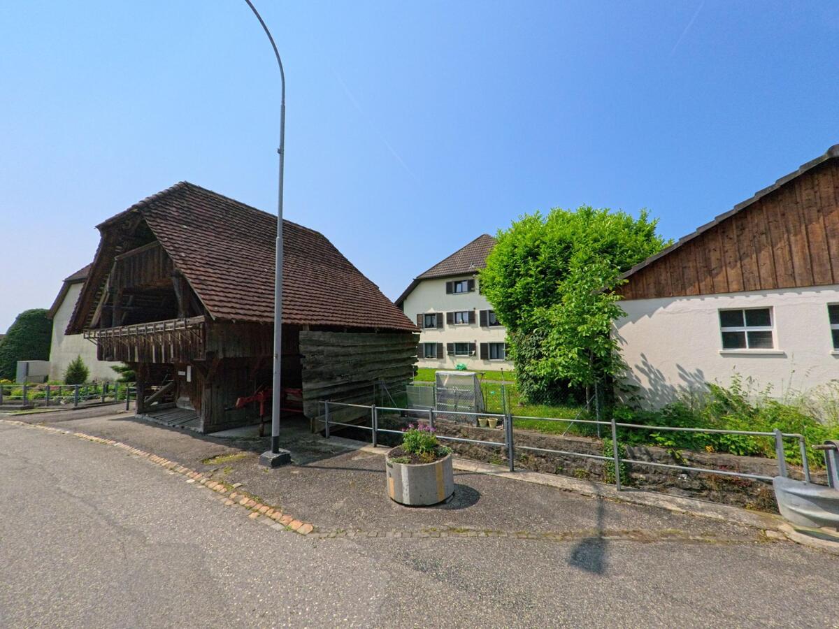 In Oberbipp (4538, Kanton Bern) steht ein gut erhaltenes Holzspeichergebäude mit Ziegeldach an einer Strasse, umgeben von Wohnhäusern und gepflegten Gärten.