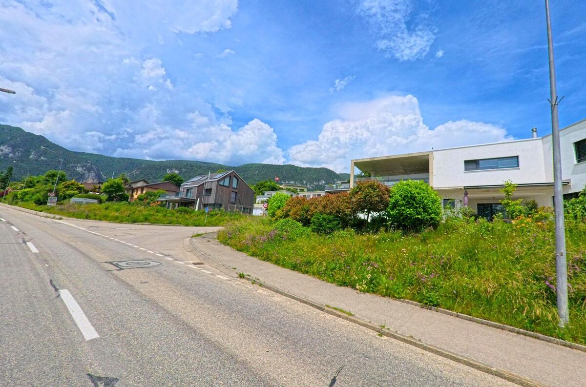 In Oberdorf (4515, Kanton Solothurn) stehen moderne Wohnhäuser mit Holz- und Putzfassaden entlang einer Kurve vor bewaldetem Jurahintergrund.