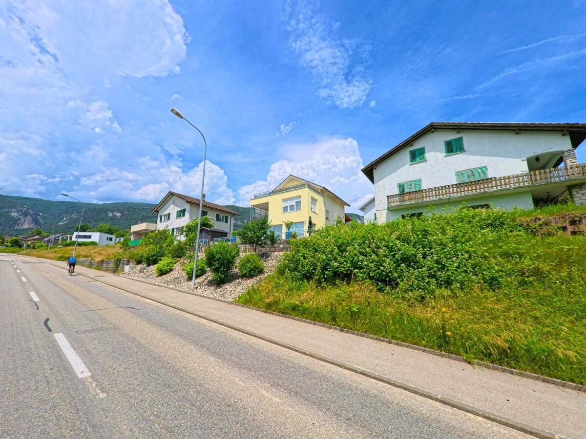 In Oberdorf (4515, Kanton Solothurn) ziehen sich Einfamilienhaeuser entlang einer leicht ansteigenden Strasse mit freiem Blick auf die Jurakette.