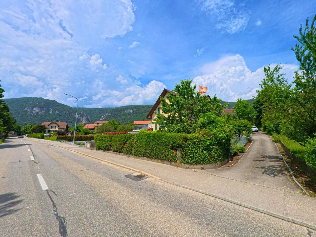 In Oberdorf (4515, Kanton Solothurn) verläuft eine ruhige Wohnstrasse mit gepflegten Vorgärten vor der Kulisse bewaldeter Hügelzüge.